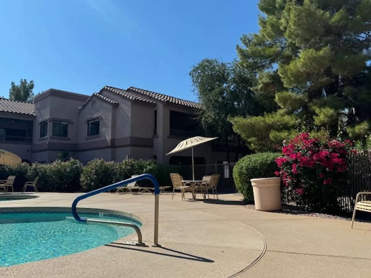 This image captures the inviting community pool area with lounge chairs, umbrellas, and flowering bushes, framed by the exterior of the building. The tranquil atmosphere is perfect for both relaxing and socializing, reflecting the resort-style amenities highlighted in the section.