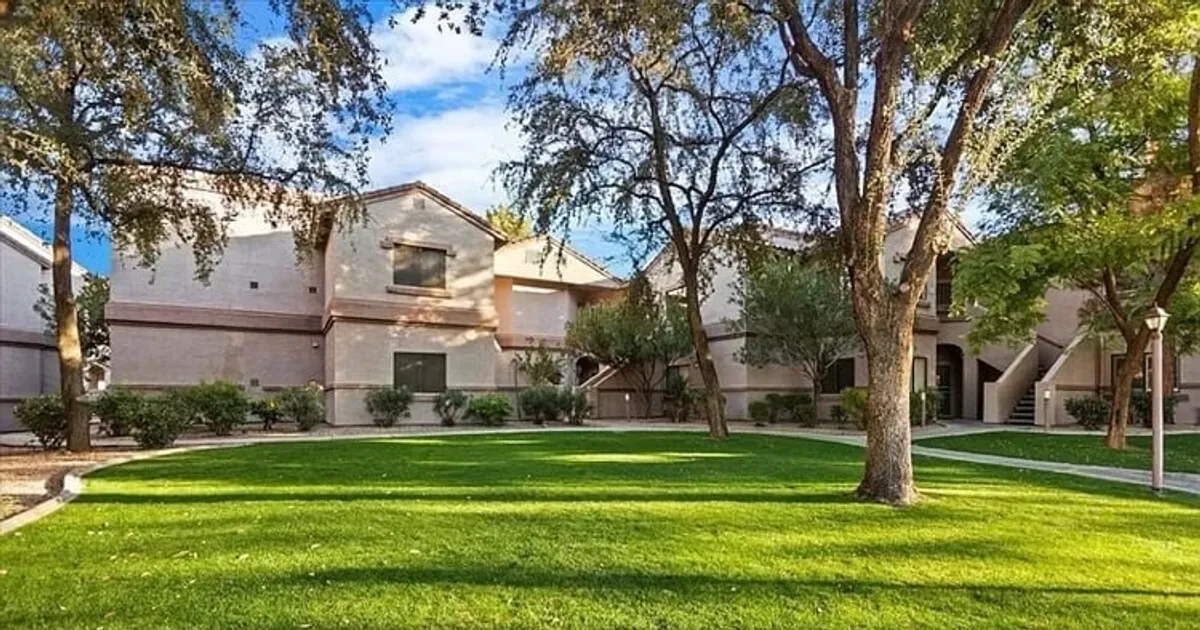 The image showcases the exterior of a modern condo building surrounded by a lush green lawn and mature trees. The inviting outdoor space features open grassy areas ideal for relaxing, picnicking, or playing, all set in a peaceful, well-maintained community environment.