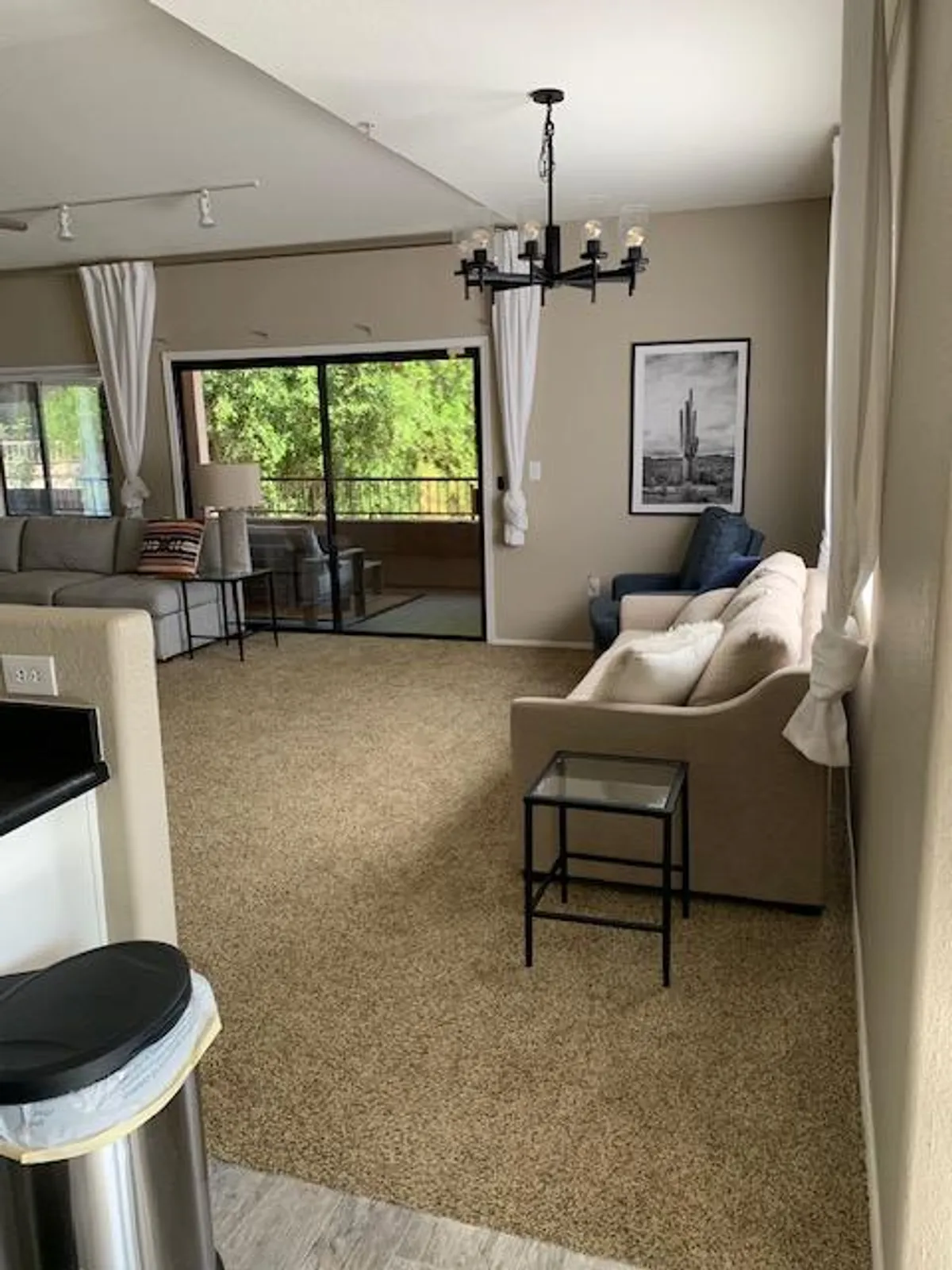 A bright, open living room featuring a modern sofa, statement chandelier, large windows that flood the space with natural light, and carefully selected artwork. The room is arranged for both relaxation and socializing, with inviting seating and a cozy reading nook by the window.