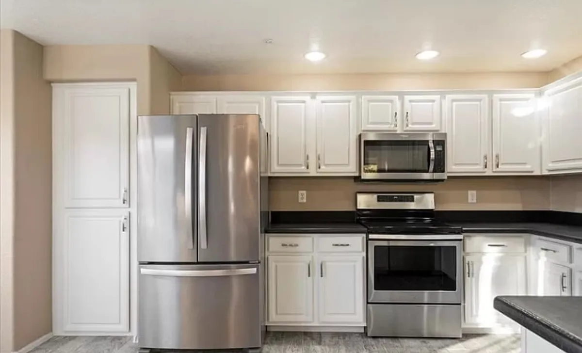 A modern kitchen scene with a gleaming stainless steel refrigerator, black countertop, and crisp white cabinetry. The space is open, functional, and ready for group gatherings or shared meals.