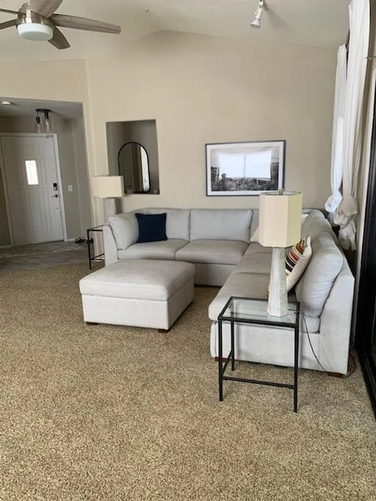 A spacious, modern living area featuring a sectional sofa, a coffee table, and framed artwork. The room is designed for relaxation and social gatherings, with ample natural light and an inviting arrangement. While not explicitly the kitchen or dining, the open layout suggests proximity and flow to a dining space.